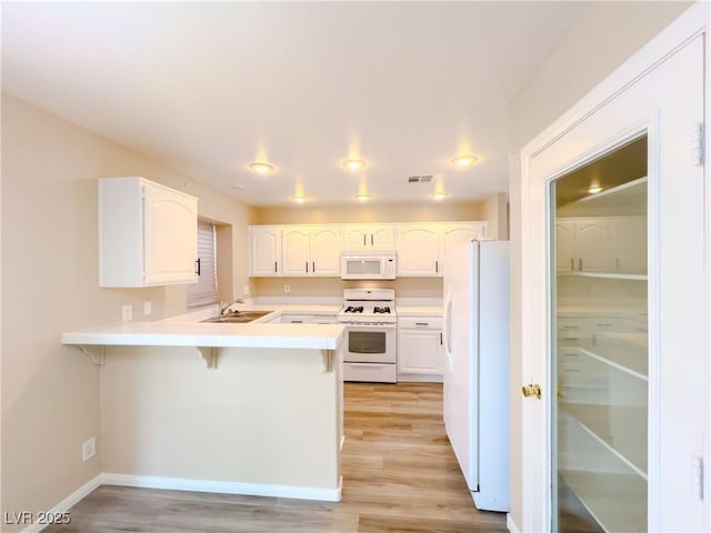 kitchen featuring visible vents, a kitchen bar, a peninsula, white cabinets, and white appliances