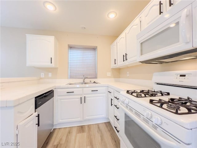 kitchen featuring light wood-type flooring, a peninsula, white cabinets, white appliances, and a sink