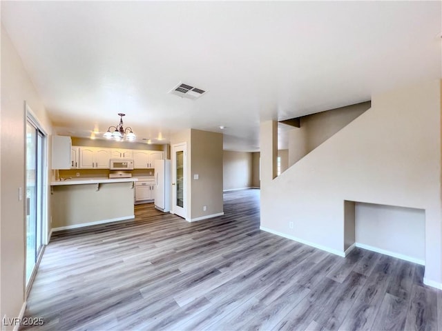 unfurnished living room with light wood-style floors, visible vents, baseboards, and a notable chandelier