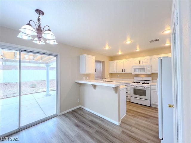 kitchen with white appliances, visible vents, a peninsula, white cabinetry, and a kitchen bar