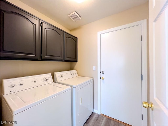 laundry area featuring washer and clothes dryer, visible vents, cabinet space, and light wood-style flooring