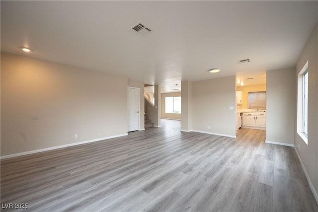 unfurnished living room with light wood-type flooring, visible vents, baseboards, and stairway