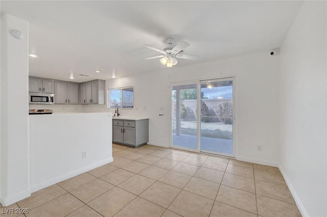 unfurnished living room featuring light tile patterned floors, a ceiling fan, baseboards, and a sink