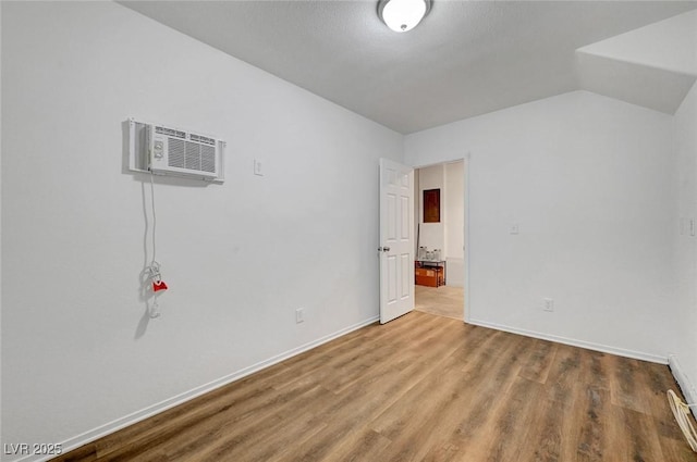 empty room featuring baseboards, lofted ceiling, a wall unit AC, and wood finished floors