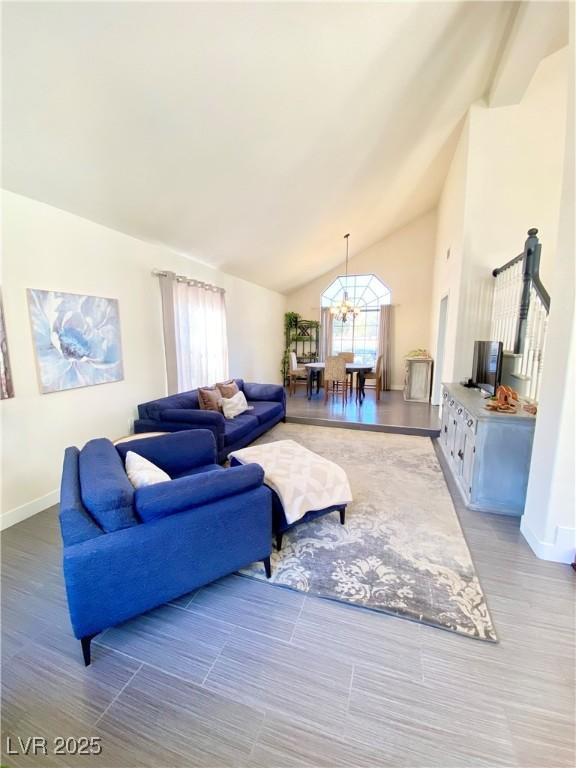 living area with baseboards, a notable chandelier, wood finished floors, and high vaulted ceiling