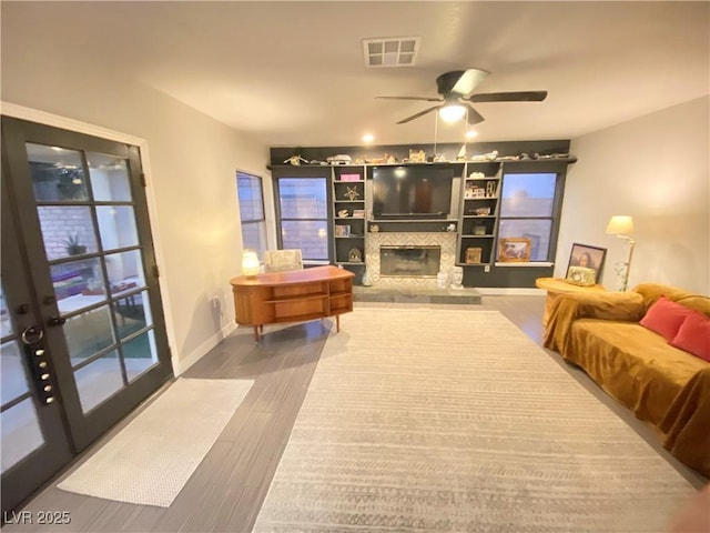 living room with wood finished floors, baseboards, visible vents, a ceiling fan, and a glass covered fireplace