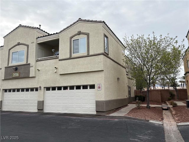 view of front facade featuring stucco siding, an attached garage, a tile roof, and fence