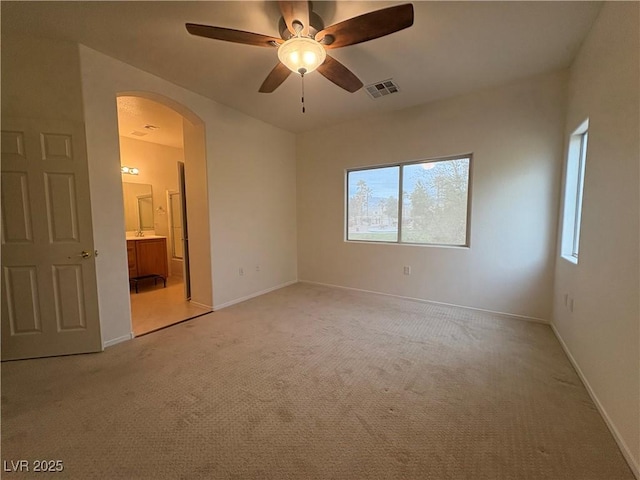 unfurnished bedroom featuring visible vents, baseboards, arched walkways, ensuite bathroom, and light colored carpet