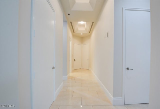 corridor featuring a tray ceiling, light tile patterned floors, and baseboards