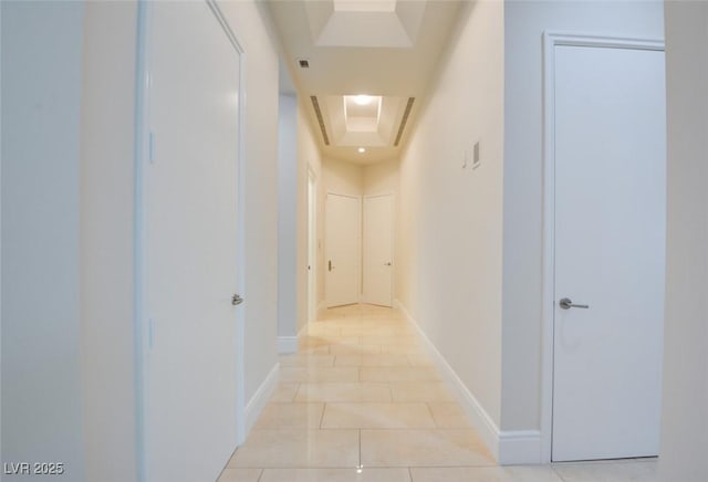 hall featuring a raised ceiling, baseboards, and light tile patterned floors