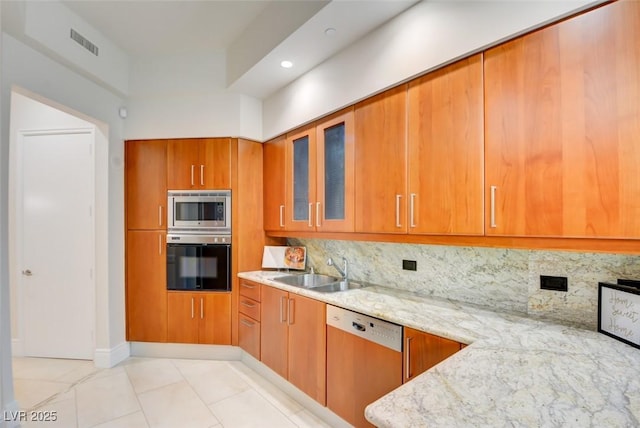 kitchen with dishwashing machine, brown cabinetry, a sink, wall oven, and stainless steel microwave