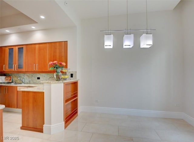 kitchen featuring brown cabinets, glass insert cabinets, baseboards, and decorative backsplash