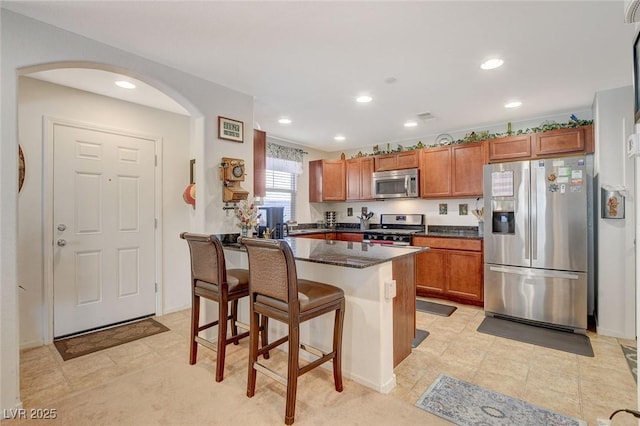 kitchen with a kitchen bar, brown cabinets, recessed lighting, stainless steel appliances, and arched walkways