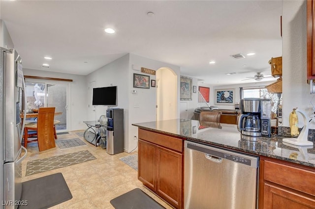 kitchen featuring visible vents, open floor plan, dark stone countertops, appliances with stainless steel finishes, and arched walkways