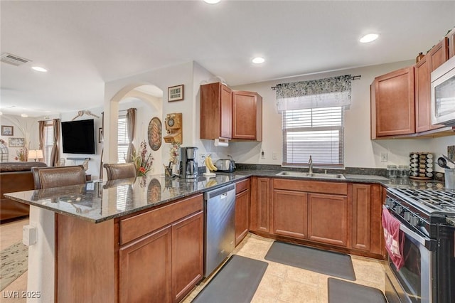 kitchen featuring visible vents, dark stone counters, arched walkways, a sink, and stainless steel appliances