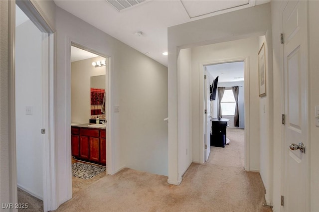 hallway with a sink, visible vents, and light colored carpet