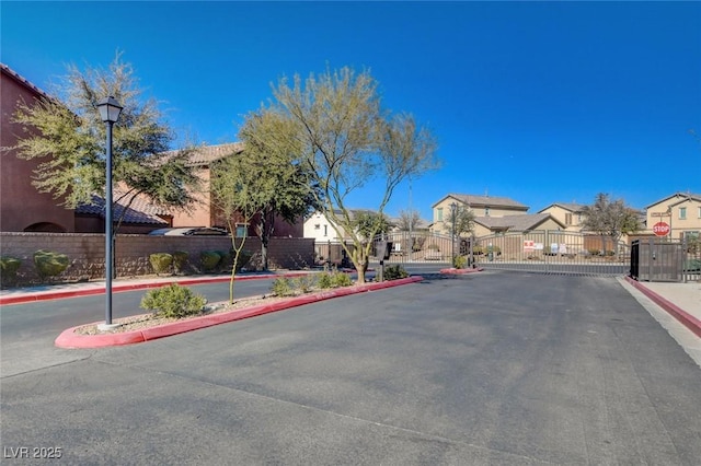 view of road featuring curbs, a gated entry, a residential view, sidewalks, and street lighting