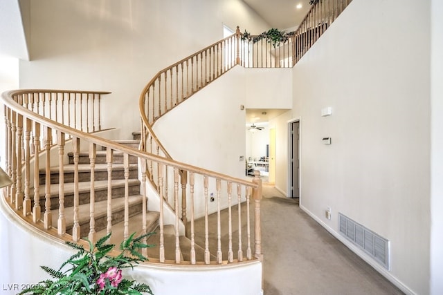 stairs featuring visible vents, baseboards, a high ceiling, and a ceiling fan