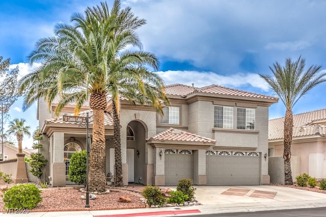 mediterranean / spanish house featuring concrete driveway, a tiled roof, an attached garage, and stucco siding