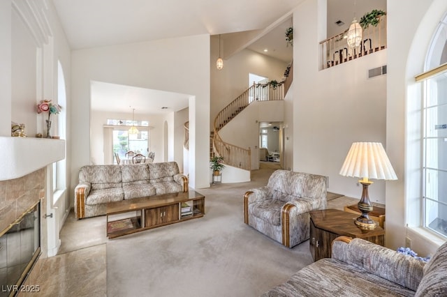 living room featuring high vaulted ceiling, stairway, carpet floors, a chandelier, and a tile fireplace