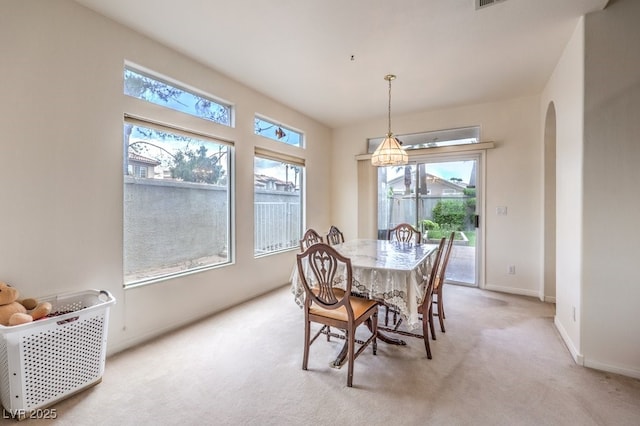 dining space featuring baseboards, light carpet, and arched walkways