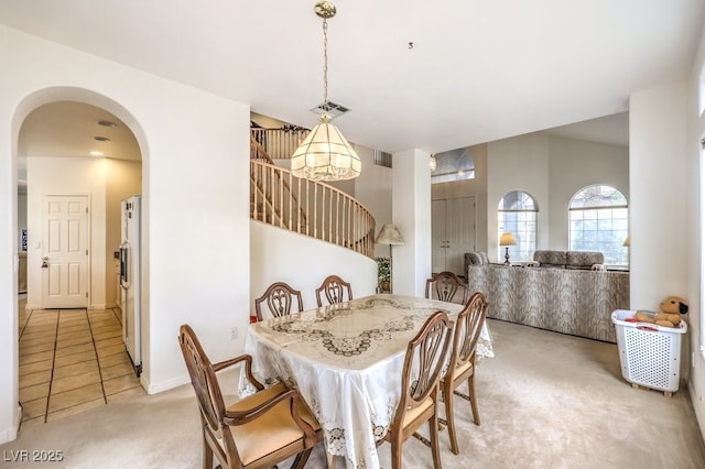 dining space with light carpet, visible vents, arched walkways, and light tile patterned floors