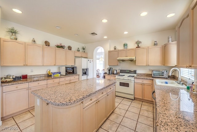 kitchen with a sink, white appliances, a kitchen island, and light brown cabinetry