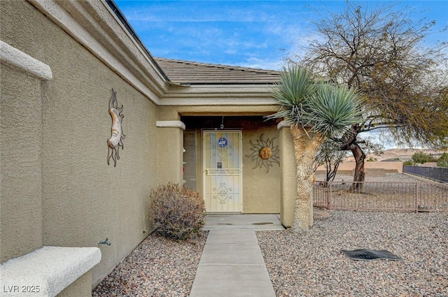 entrance to property featuring a tiled roof, fence, and stucco siding