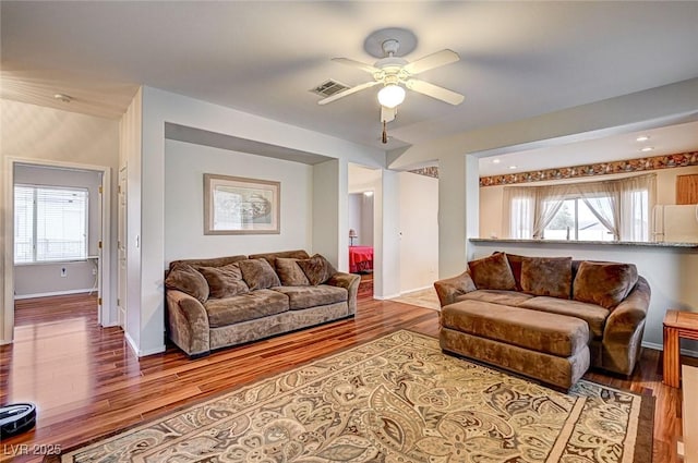 living room with ceiling fan, wood finished floors, visible vents, and baseboards