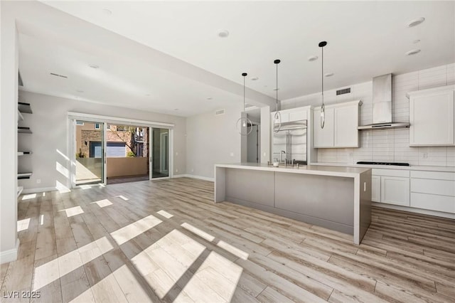 kitchen with visible vents, light wood-style flooring, open floor plan, wall chimney exhaust hood, and tasteful backsplash