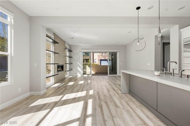 kitchen with a sink, light wood-type flooring, decorative light fixtures, and light countertops