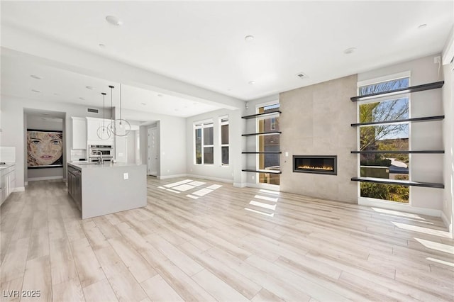 living area with visible vents, a tile fireplace, light wood-type flooring, and baseboards