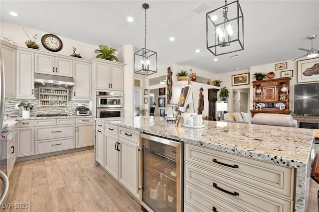 kitchen with gas stovetop, wine cooler, under cabinet range hood, double oven, and open floor plan