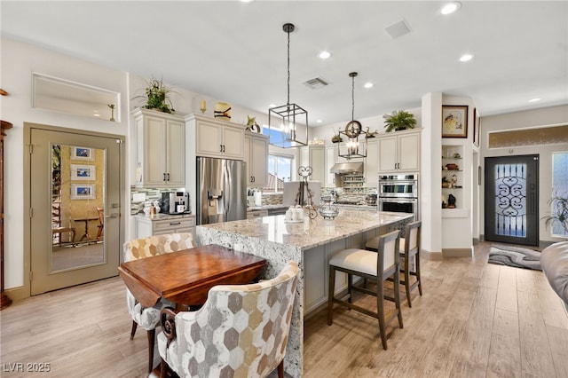 kitchen featuring light wood finished floors, visible vents, backsplash, under cabinet range hood, and stainless steel appliances