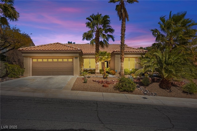 mediterranean / spanish-style house featuring concrete driveway, a tiled roof, a garage, and stucco siding