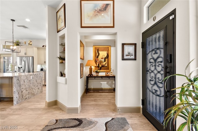 entrance foyer with a chandelier, visible vents, baseboards, and light wood-style floors