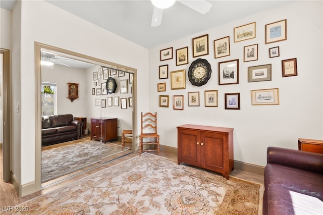 living area featuring wood finished floors, baseboards, and ceiling fan