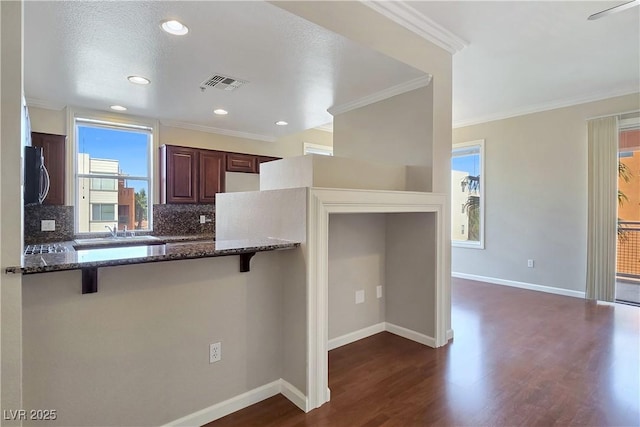 kitchen featuring visible vents, dark stone countertops, a breakfast bar, and dark wood-type flooring