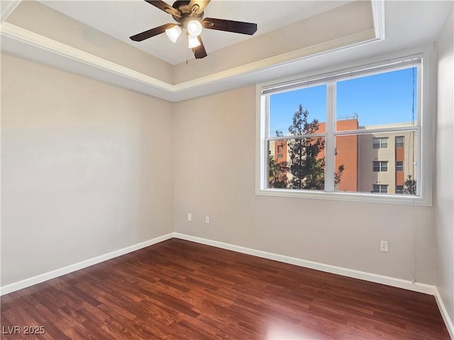 empty room featuring ceiling fan, a tray ceiling, baseboards, and wood finished floors