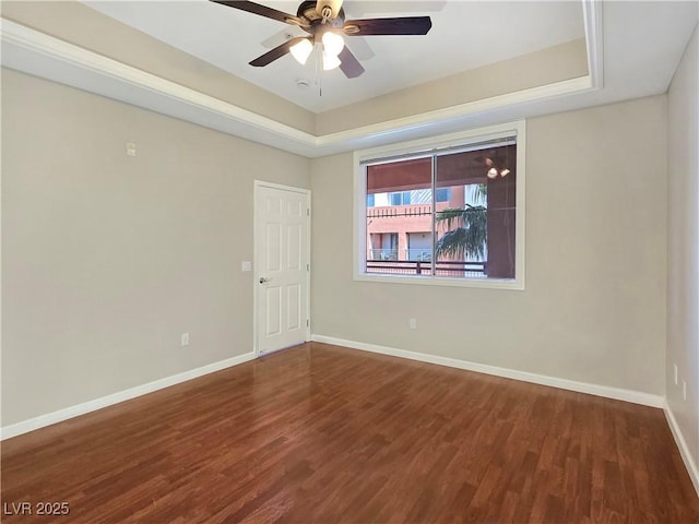 unfurnished room featuring a raised ceiling, wood finished floors, and baseboards