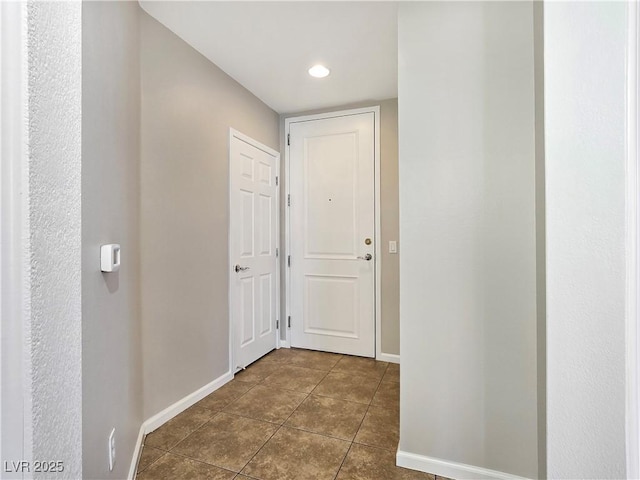 hallway featuring baseboards and dark tile patterned flooring