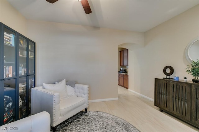 sitting room with baseboards, arched walkways, and ceiling fan