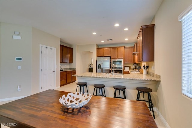 kitchen featuring a sink, recessed lighting, appliances with stainless steel finishes, a peninsula, and light stone countertops