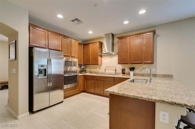 kitchen featuring stainless steel appliances, a breakfast bar, a sink, a peninsula, and wall chimney exhaust hood