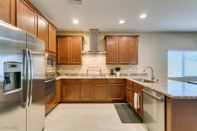 kitchen with a sink, stainless steel appliances, a peninsula, wall chimney exhaust hood, and brown cabinetry