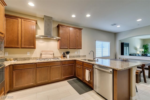 kitchen featuring visible vents, a peninsula, stainless steel appliances, wall chimney exhaust hood, and a sink