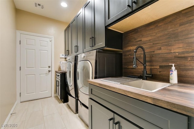 clothes washing area with visible vents, a sink, cabinet space, separate washer and dryer, and wooden walls