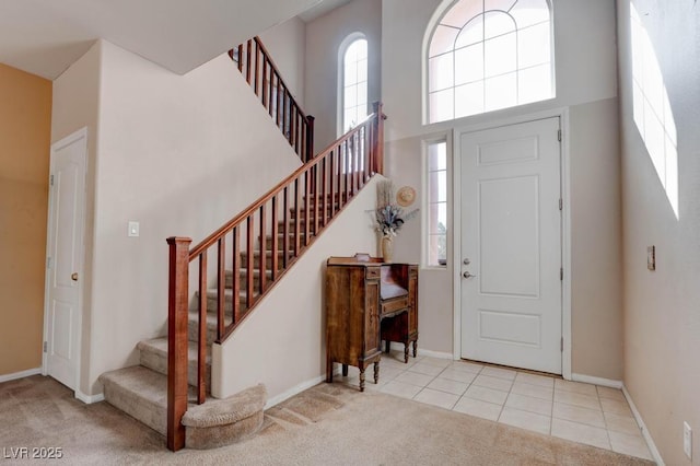 carpeted foyer featuring baseboards, a towering ceiling, stairs, and tile patterned flooring