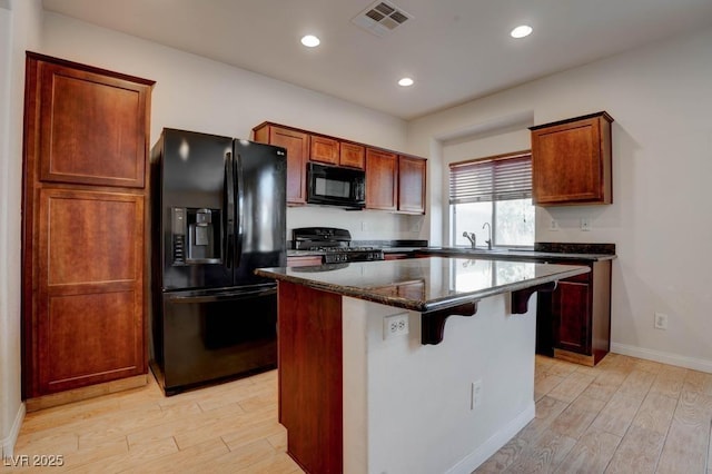 kitchen with light wood-type flooring, visible vents, black appliances, and a center island