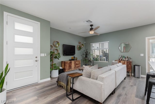 living area featuring visible vents, baseboards, ceiling fan, and light wood finished floors